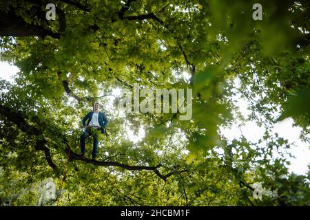 Un uomo d'affari sorridente che usa lo smartphone appeso alla corda nel parco Foto Stock