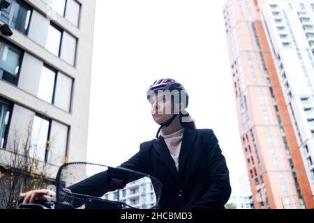 Donna d'affari che indossa casco in bicicletta in città Foto Stock