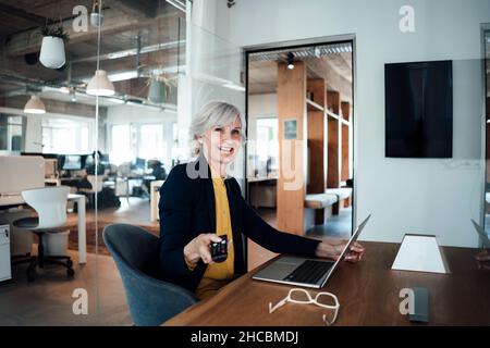 Donna d'affari anziana che mette nota adesiva sulla parete di vetro Foto Stock