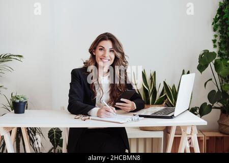 Donna d'affari sorridente con smartphone che fa lavoro di ufficio Foto Stock
