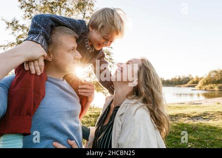 Donna sorridente che guarda l'uomo che porta il figlio sulle spalle nel parco Foto Stock