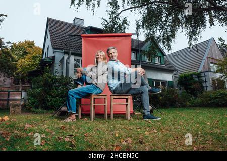 Coppia sorridente seduta su sgabelli di fronte allo sfondo Foto Stock