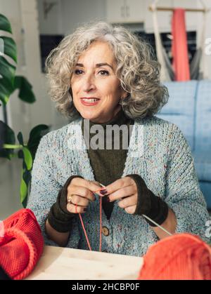 Donna anziana registrazione mentre cucito e maglieria a casa Foto Stock
