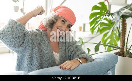 Donna anziana sorridente con bandana rilassante sul divano a casa Foto Stock