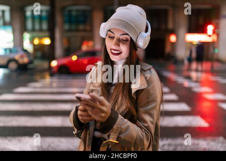 Giovane donna con cuffie che utilizzano lo smartphone in città Foto Stock