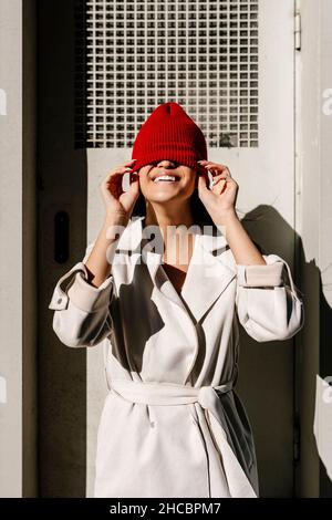 Donna giocosa che ricopre il viso con cappello a maglia in giornata di sole Foto Stock