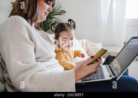 Madre che usa il laptop con la figlia a casa Foto Stock