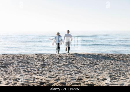 Uomo e donna che corrono verso il mare in spiaggia Foto Stock