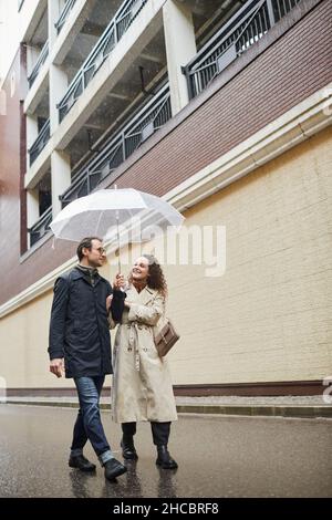 Lungo scatto verticale di elegante uomo e donna caucasica che trascorrono il tempo insieme all'aperto camminando sotto l'ombrello Foto Stock