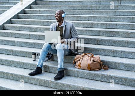 Uomo d'affari con cuffie per realtà virtuale che utilizzano un computer portatile seduto su gradini Foto Stock