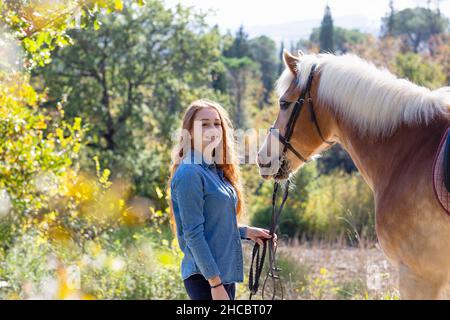 Donna sorridente in piedi con cavallo al prato in giorno di sole Foto Stock