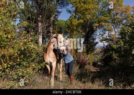 Giovane donna con cavallo che cammina nel prato in giorno di sole durante il fine settimana Foto Stock