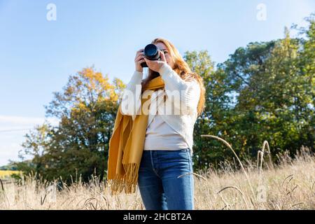 Giovane donna fotografata con la macchina fotografica mentre si trova in erba Foto Stock