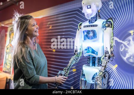 Un tecnico felice che agita le mani con il robot umano in officina Foto Stock