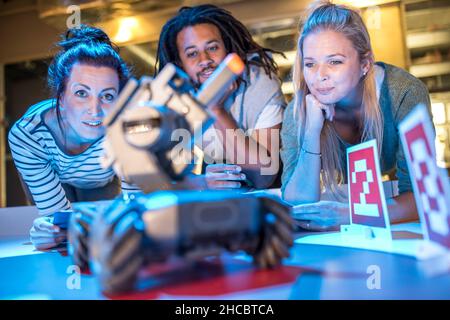 Giovane tecnico con colleghi che guardano al carro armato automatizzato di combattimento robotico in officina Foto Stock