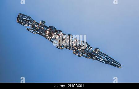 Fiocco di neve ad ago reale ad alto ingrandimento. Foto macro di un piccolo cristallo di neve rigata, fiocco di neve che risplendente su sfondo blu scuro. Foto Stock