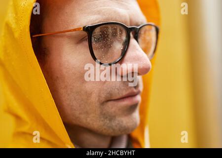 Primo piano ritratto di moderno uomo caucasico con impermeabile giallo in piedi all'aperto guardando lontano Foto Stock