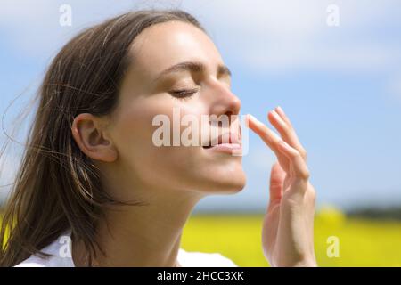 Ritratto di una bella donna che mette crema idratante sulla guancia in un campo Foto Stock