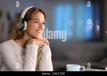 Donna felice che indossa le cuffie sorridenti ascoltando la musica a casa di notte Foto Stock