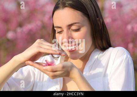 Donna felice che tiene e protegge il fiore in un campo rosa Foto Stock