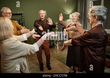 Due uomini di età e tre donne di buon aspetto in cerchio in decorato con luci soggiorno contro muro verde, ballando e divertirsi insieme Foto Stock