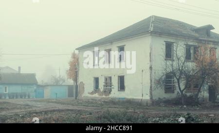 Una casa in legno abbandonata a due piani sulla strada in una giornata di nebbia Foto Stock