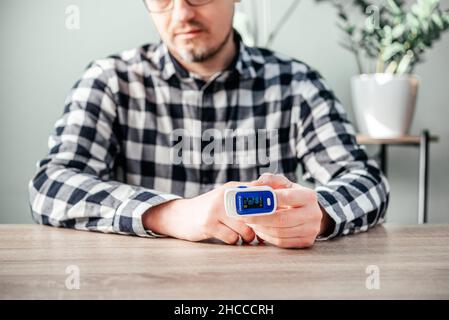 Un uomo che controlla il livello di ossigeno a casa con ossimetro domestico, paziente che misura l'ossigeno nel sangue con ossimetro Foto Stock