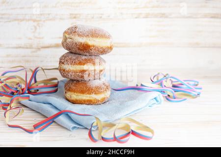Stack di ciambelle Berliner chiamato anche Krapfen con streamers partito su un tovagliolo e un tavolo di legno chiaro, pasticceria fritta profonda per il carnevale e Capodanno Foto Stock