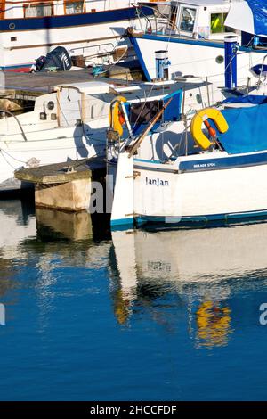 Primo piano dettaglio delle barche ancorate al porto turistico nel molo interno del porto di Arbroath e i riflessi che gettano in acqua in una tranquilla giornata di sole. Foto Stock