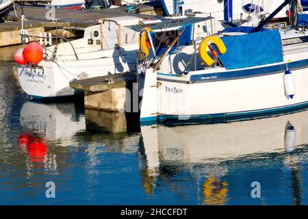 Primo piano dettaglio delle barche ancorate al porto turistico nel molo interno del porto di Arbroath e i riflessi che gettano in acqua in una tranquilla giornata di sole. Foto Stock