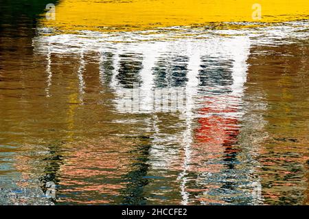Il riflesso di una piccola barca gialla, distorta ma ancora riconoscibile, nelle acque relativamente calme del porto di Arbroath, Angus, Scozia, Regno Unito. Foto Stock