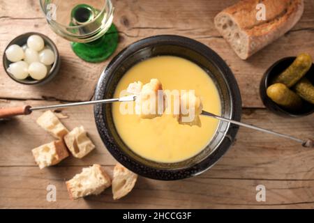 Fonduta di formaggio fuso con pane su forchette lunghe, sottaceti e vino su un rustico tavolo di legno, piatto tradizionale di nuovo anno dalla Svizzera, spazio copia, Foto Stock