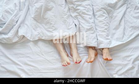 I giovani uomini e le donne si trovano nel letto che attacca le gambe fuori dal foglio Foto Stock