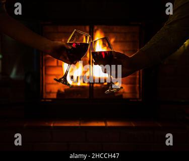 Primo piano della coppia mani che si accoppiano bicchieri di vino vicino al caldo camino in casa Foto Stock