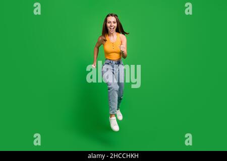 Foto a tutta lunghezza di giovane funky bruna signora run indossare top jeans scarpe isolate su sfondo verde Foto Stock