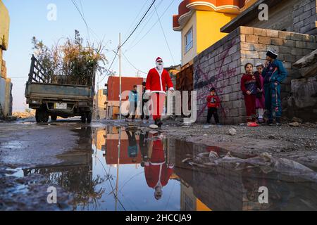 Un uomo vestito da Babbo Natale cammina vicino ai bambini nella città vecchia di Mosul.un'iniziativa lanciata da volontari iracheni della Mosul Eye Foundation per piantare migliaia di alberi nella città devastata dalla guerra di Mosul, con l'obiettivo di rendere più verde Mosul e combattere la desertificazione, Hanno distribuito 100 alberi diversi alle case della città vecchia di Mosul come parte di un progetto volto a piantare 5.000 alberi in tutta la città settentrionale di Mosul, che ancora soffre per la distruzione e la devastazione lasciate dalla guerra contro l'Isis. Foto Stock