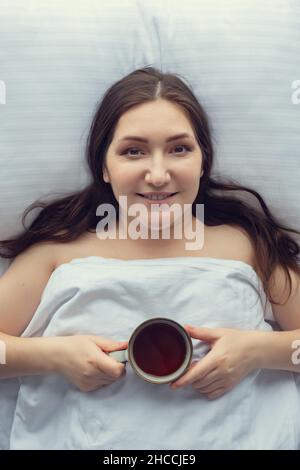 donna brunetta con una tazza di caffè a letto, vista dall'alto Foto Stock