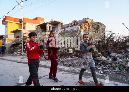 Mosul, Iraq. 24th Dic 2021. I bambini tengono alberi dopo che un uomo vestito come Babbo Natale distribuiscono loro vicino alle macerie nella città vecchia di Mosul.un'iniziativa lanciata da volontari iracheni dalla Fondazione occhio di Mosul piantare migliaia di alberi nella città devastata dalla guerra di Mosul, Allo scopo di rendere più verde Mosul e combattere la desertificazione, distribuivano 100 alberi diversi alle case del centro storico di Mosul nell'ambito di un progetto volto a piantare 5.000 alberi in tutta la città settentrionale di Mosul, Che soffre ancora della distruzione e della devastazione lasciate dalla guerra contro l'ISI Foto Stock