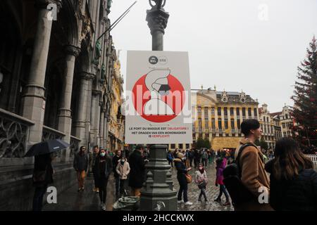 Bruxelles, Belgio. 27th Dic 2021. La gente cammina davanti a un poster di uso obbligatorio di maschere facciali nella Grand Place di Bruxelles, Belgio, il 27 dicembre 2021. Il Belgio ha imposto misure supplementari per rallentare la diffusione della variante Omicron, che sta causando un picco di casi in tutta Europa. A partire dal 26 dicembre, i mercatini natalizi al coperto, i cinema, i teatri e le sale da concerto sono chiusi, ma i musei e le biblioteche rimangono aperti. Credit: Zheng Huansong/Xinhua/Alamy Live News Foto Stock