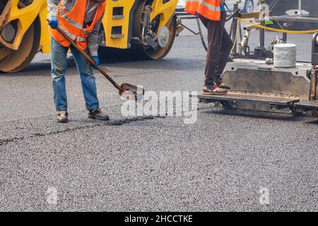 Gli operatori stradali stanno riparando un tratto di strada con una pala, un'asfaltatrice e un rullo, posando uno strato di nuovo asfalto caldo sulla carreggiata. Spazio di copia. Foto Stock
