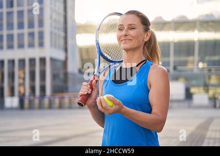 Bella donna di mezza età, professionista giocatore di tennis che tiene racket tennis e una palla pronta per giocare a tennis in città Foto Stock