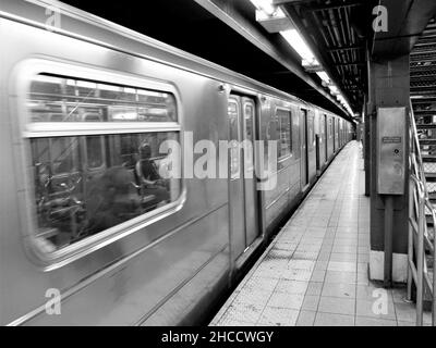 Immagine in scala di grigi del treno in movimento con i passeggeri nella stazione ferroviaria Foto Stock