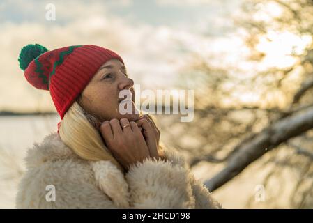 ritratto di una donna bionda in un cappello rosso su un lago innevato freddo invernale. Foto Stock