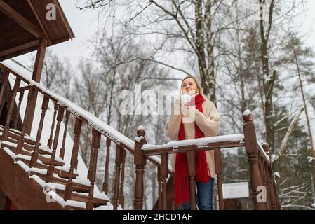donna bionda in un cappello rosso sul portico bere caffè inverno freddo Foto Stock