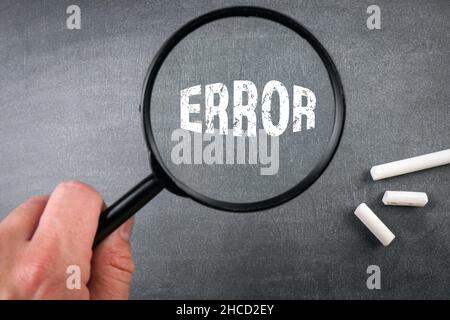Concetto di errore. Lente d'ingrandimento in mano di un uomo. sfondo della tavola di gesso. Foto Stock