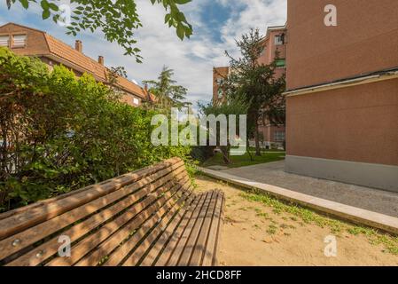 panca di legno situata in un'area ricreativa con siepi e alberi da giardino in aree comuni di un edificio residenziale Foto Stock