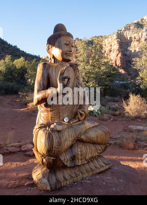 Statua del Buddha di Shakyamuna in legno intagliato con scogliere di arenaria rossa sullo sfondo. Fotografato all'Amitubha Stupa and Peace Park di Sedona, Arizona. Foto Stock