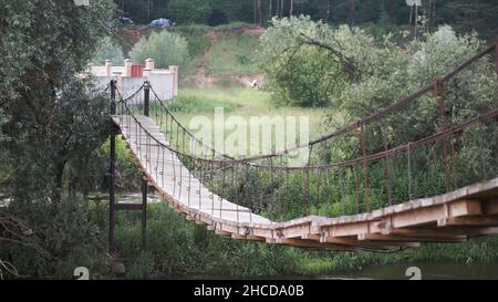 Ponte di legno nel parco. Clip. Passerella in corda per la foresta pluviale. Vecchio ponte di legno per attraversare la palude. Ponte sospeso in legno attraverso il fiume fino all'autum Foto Stock
