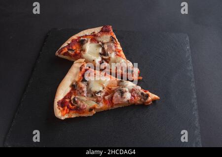 fette di pizza appena sfornata su una lavagna nera su sfondo scuro Foto Stock