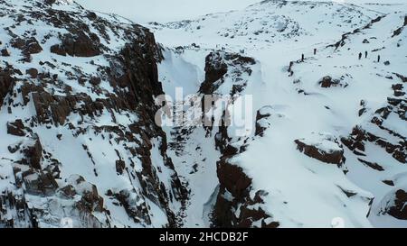 Antenna di rocce ripide ricoperte di neve bianca dal mare blu, bellezza della natura invernale concetto. Volo su una splendida costa rocciosa nella stagione invernale. Foto Stock